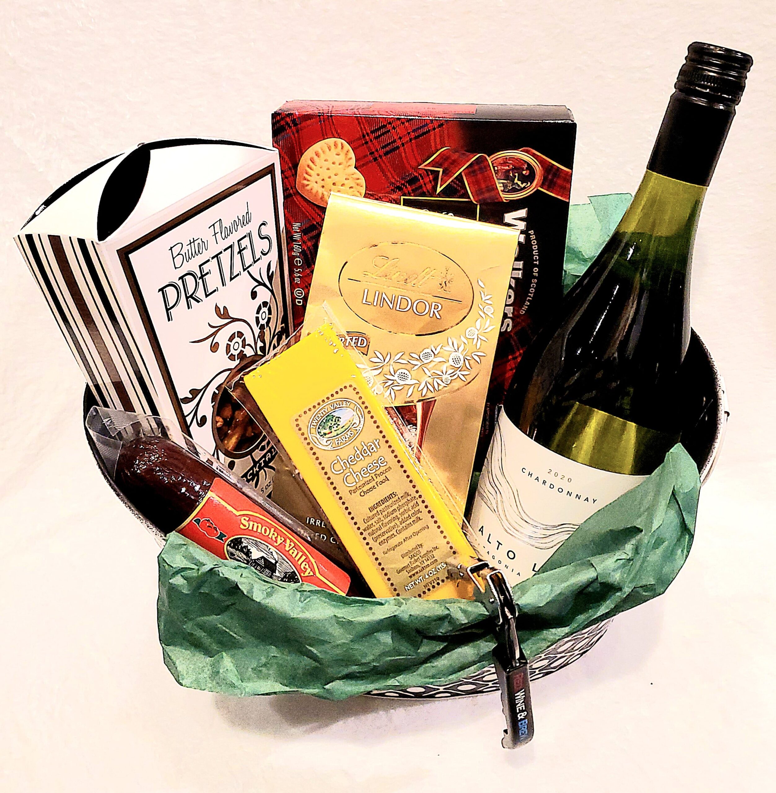 A basket with one wine bottle and assorted snacks.